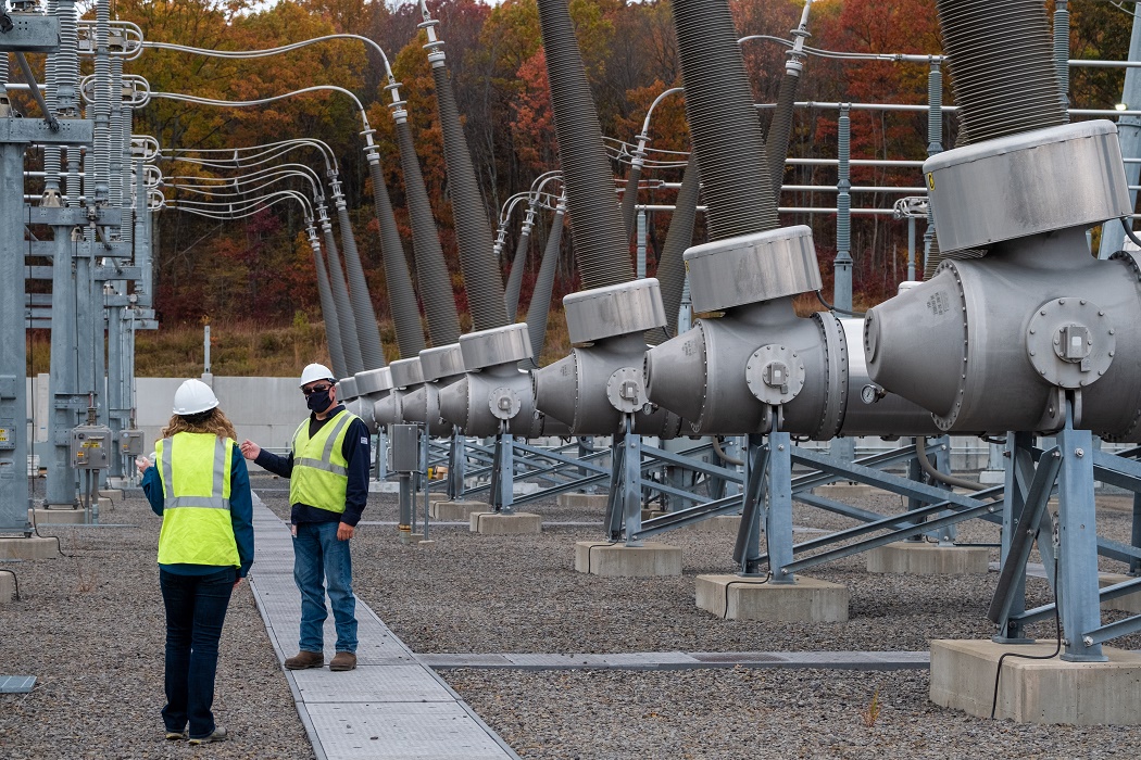 2 employees standing amid a large electrical substation