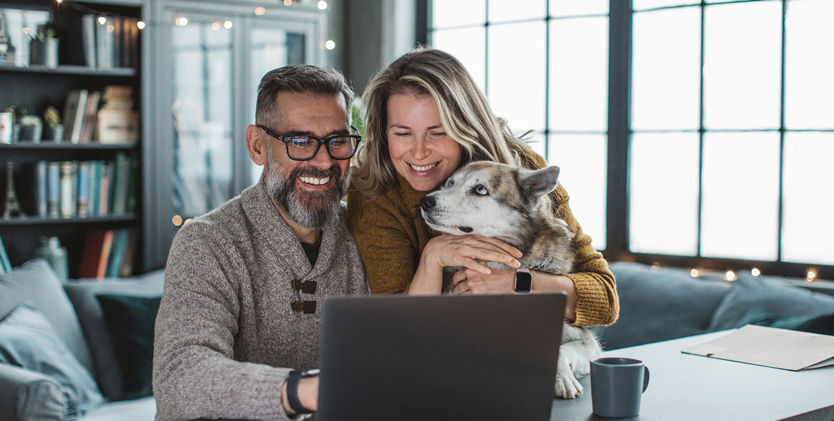 husband and wife with their dog looking at laptop with smile