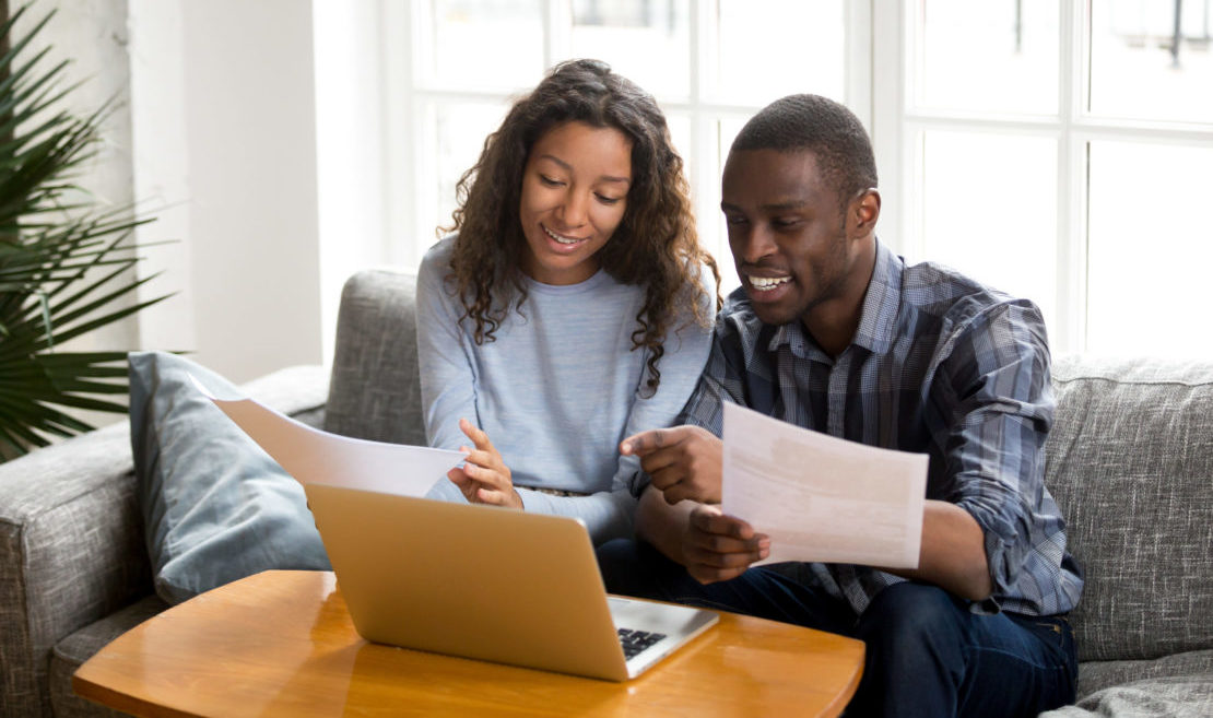 Young couple sitting on sofa looking at paperwork and laptop