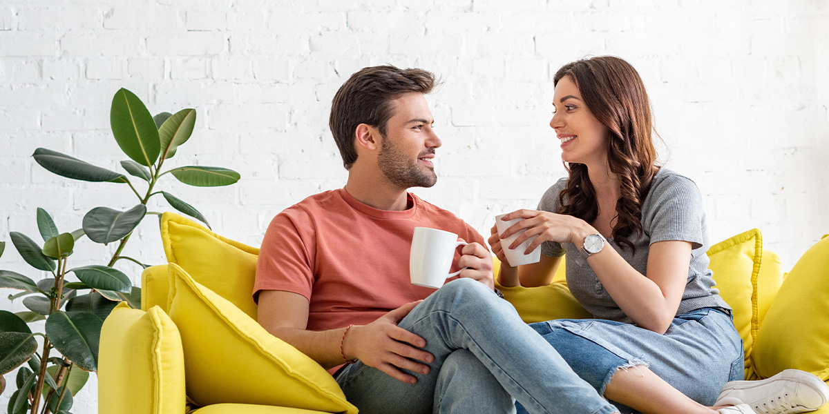 Couple sits on couch with coffee mugs