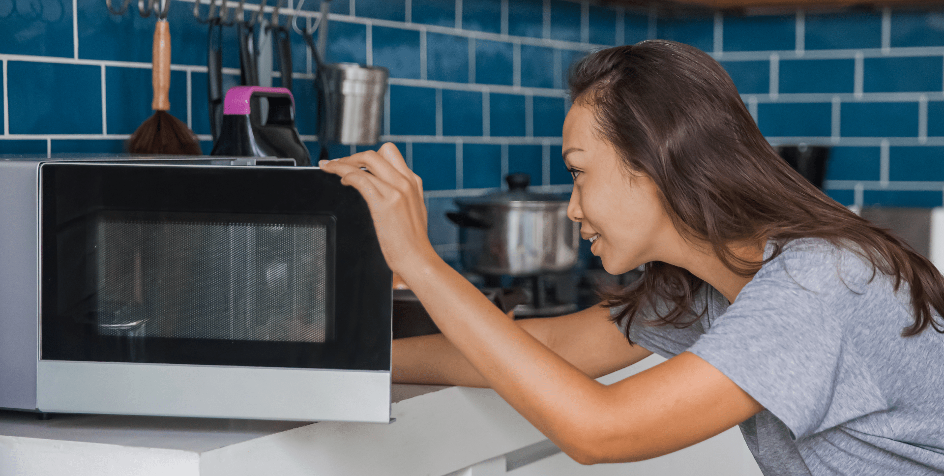 A woman reaches into a microwave to remove a container.