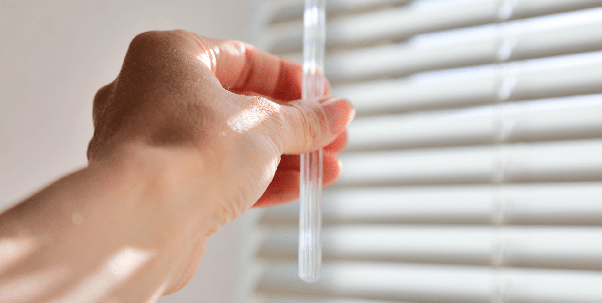 A hand closes Venetian blinds using the adjusting rod.