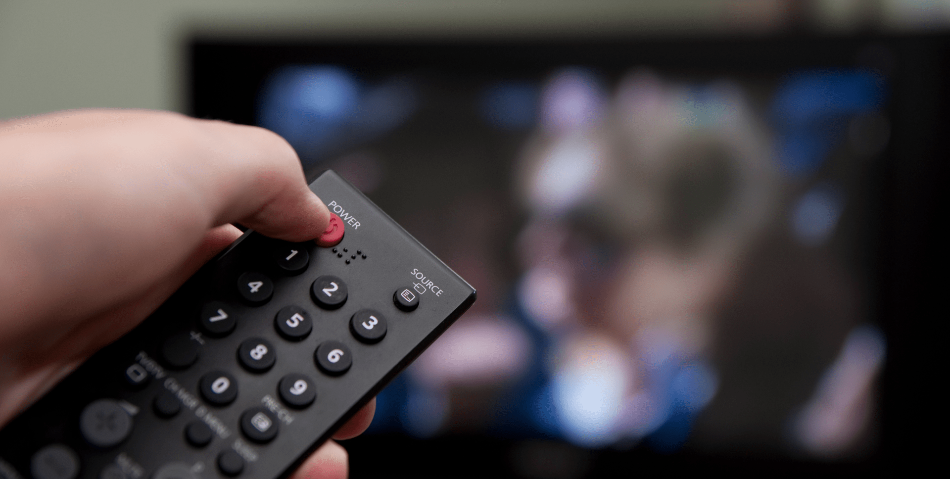 A hand pointing a remote at the TV and pressing the power button