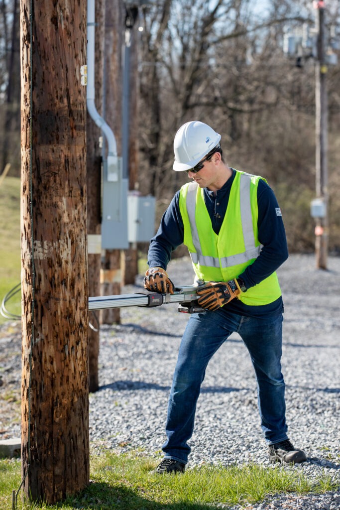 employee using resistance drill to help measure utility pole decay and identify whether replacement is necessary.