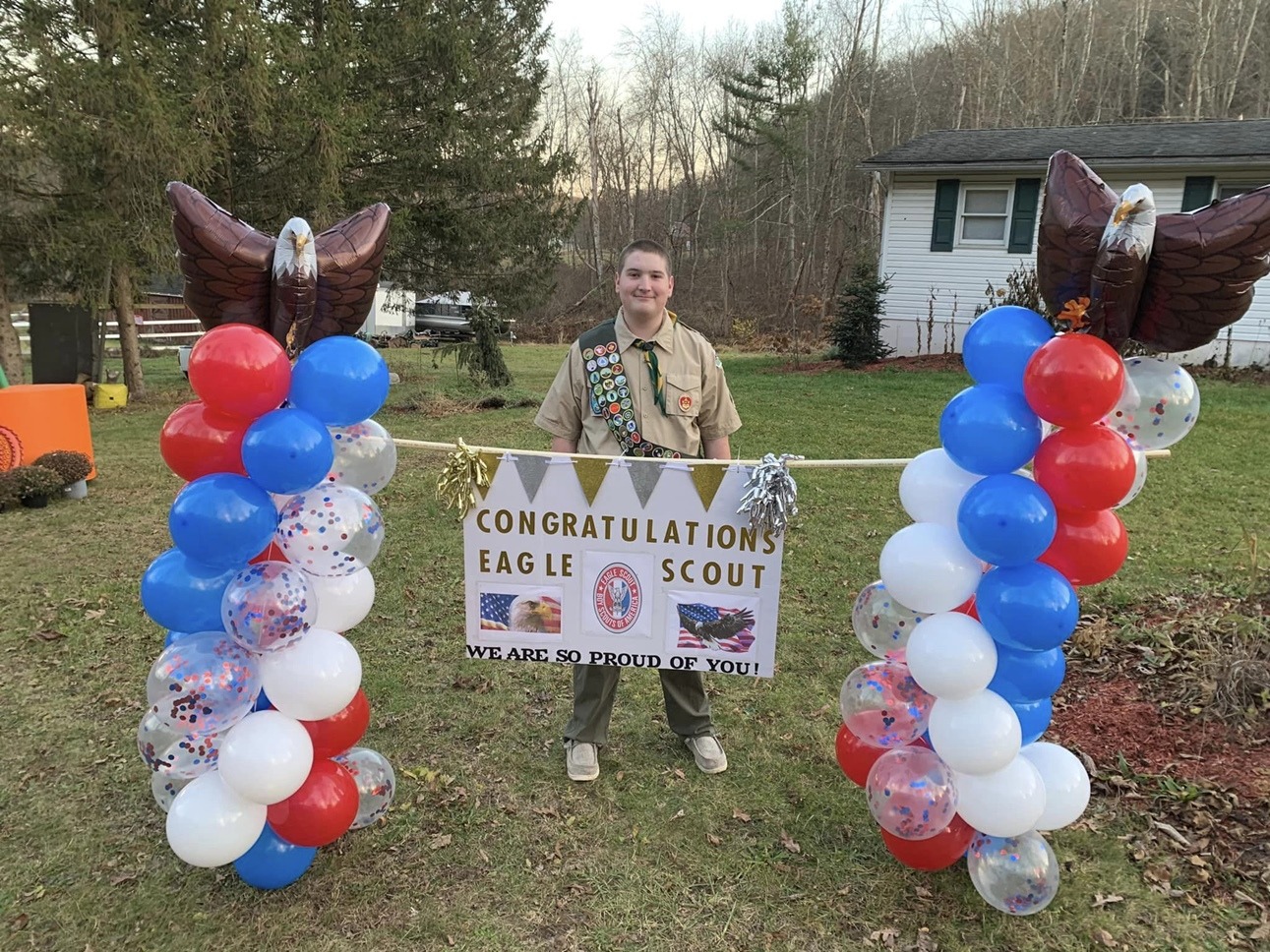 Boy Scout Garrett Hawk stands in his yard displaying a banner that let's the world know he has attained the rank of Eagle Scout.