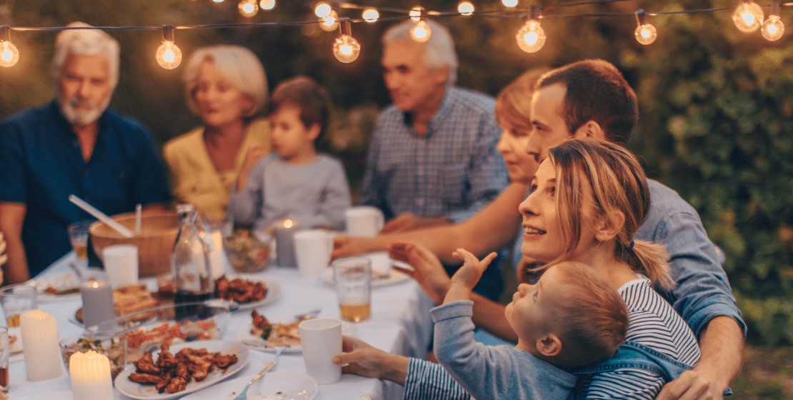 A family gathered around an outdoor dinner table with string lights above