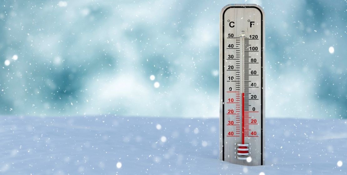 Photo of a thermometer in the snow in front of a snowy background.