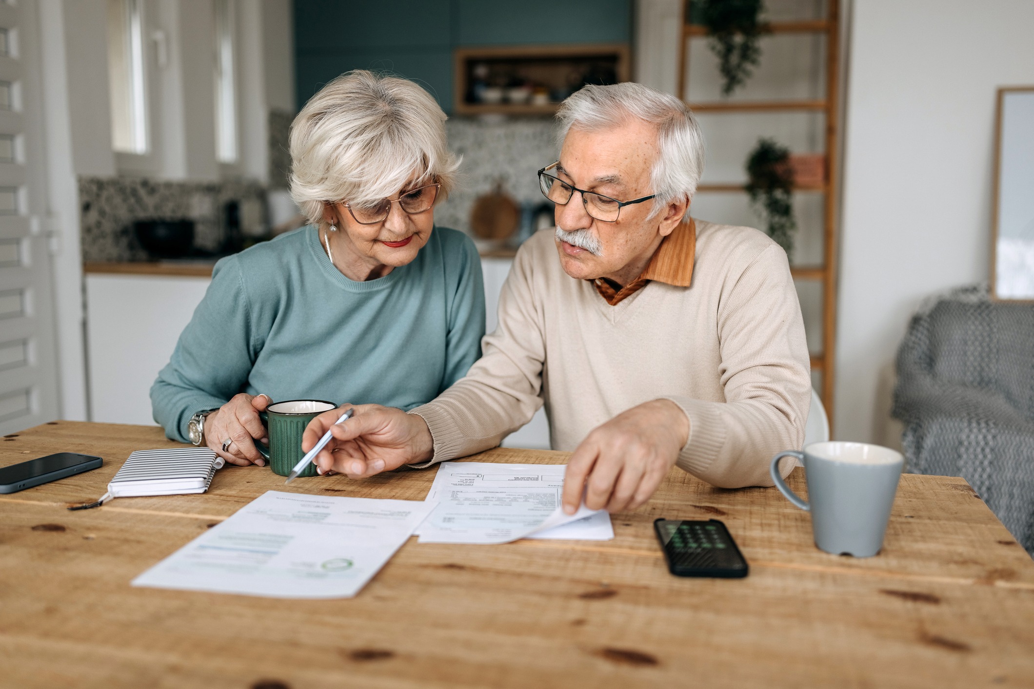 Older couple reviewing utility bills at home Senior couple sitting at a kitchen table reviewing their electric bill and paperwork together