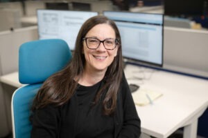 woman smiling, computer screen behind her 